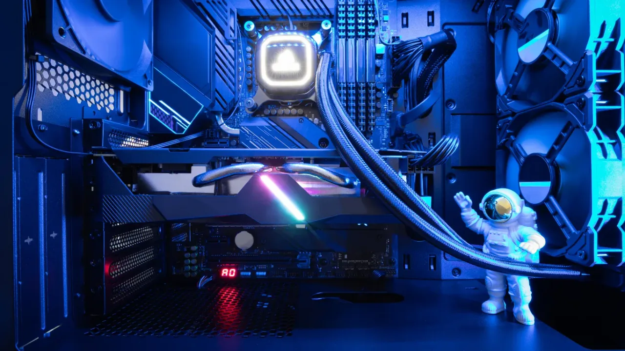 A detailed close-up shot inside a custom PC case bathed in cool blue LED light, showing a graphics card with an RGB light strip, an AIO liquid CPU cooler, cooling fans, and a small astronaut figurine waving on the power supply shroud, illustrating the creative process to build a gaming PC.