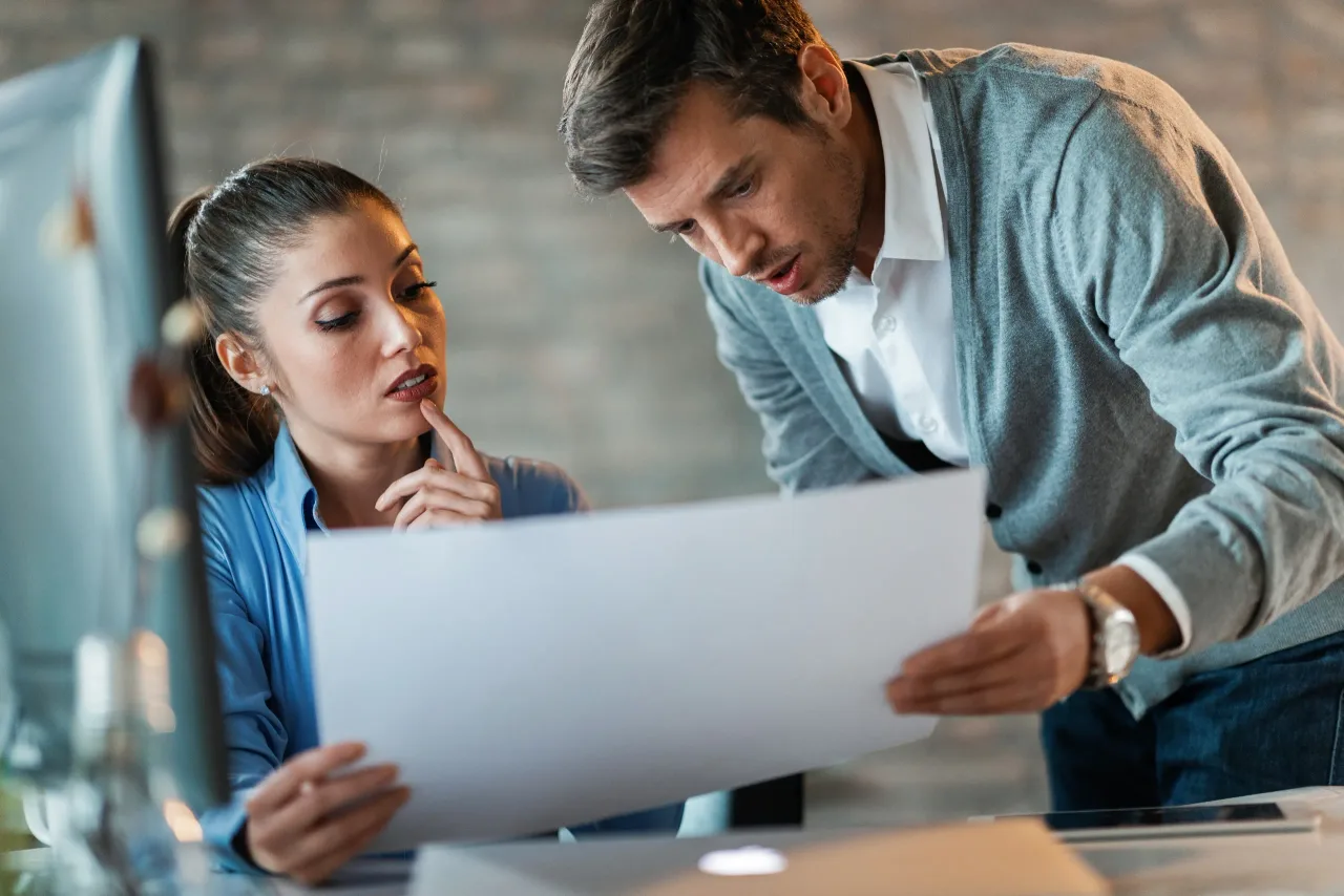 two entrepreneurs cooperating while reading blueprints working together office
