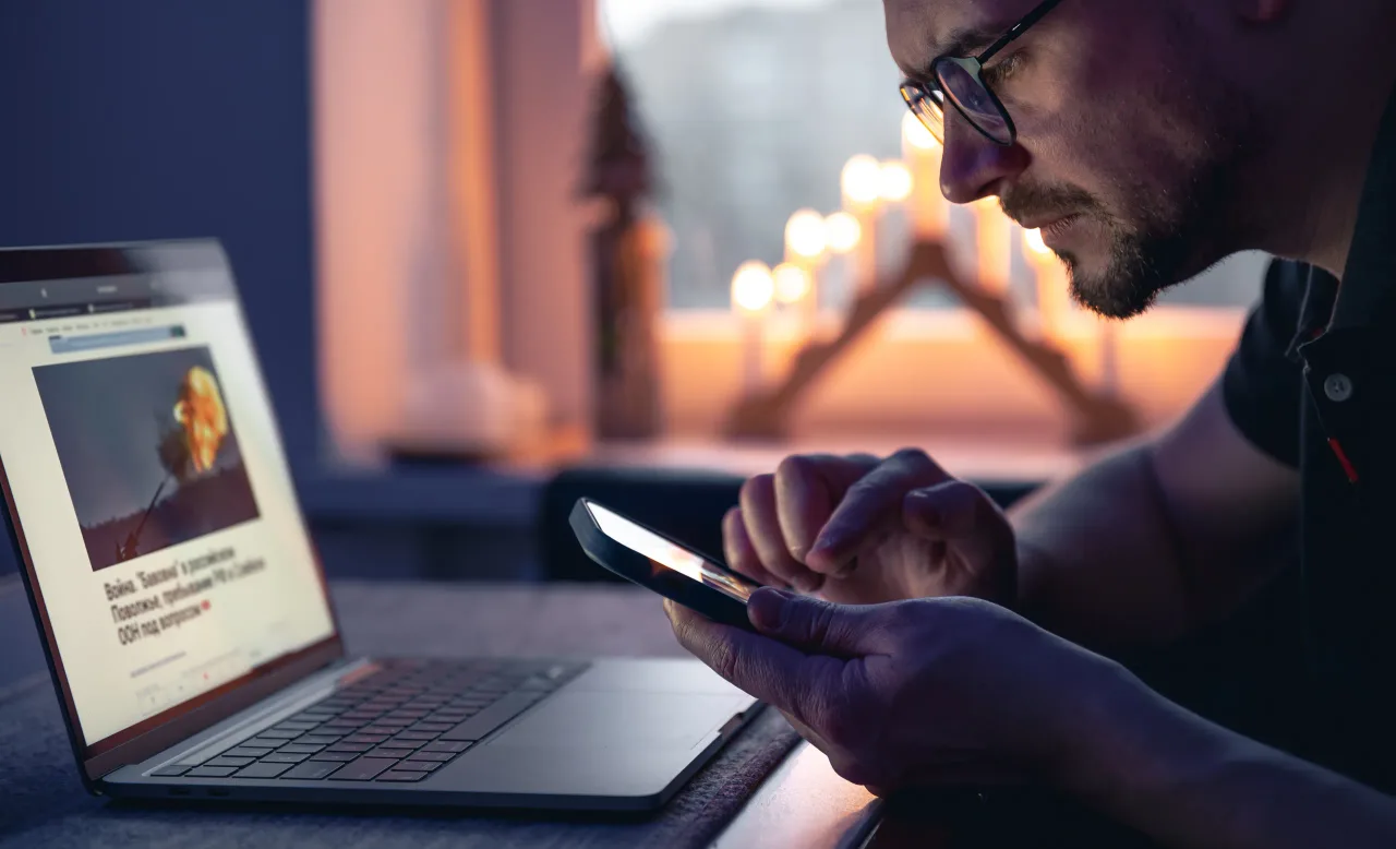 man with smartphone sits front laptop late night