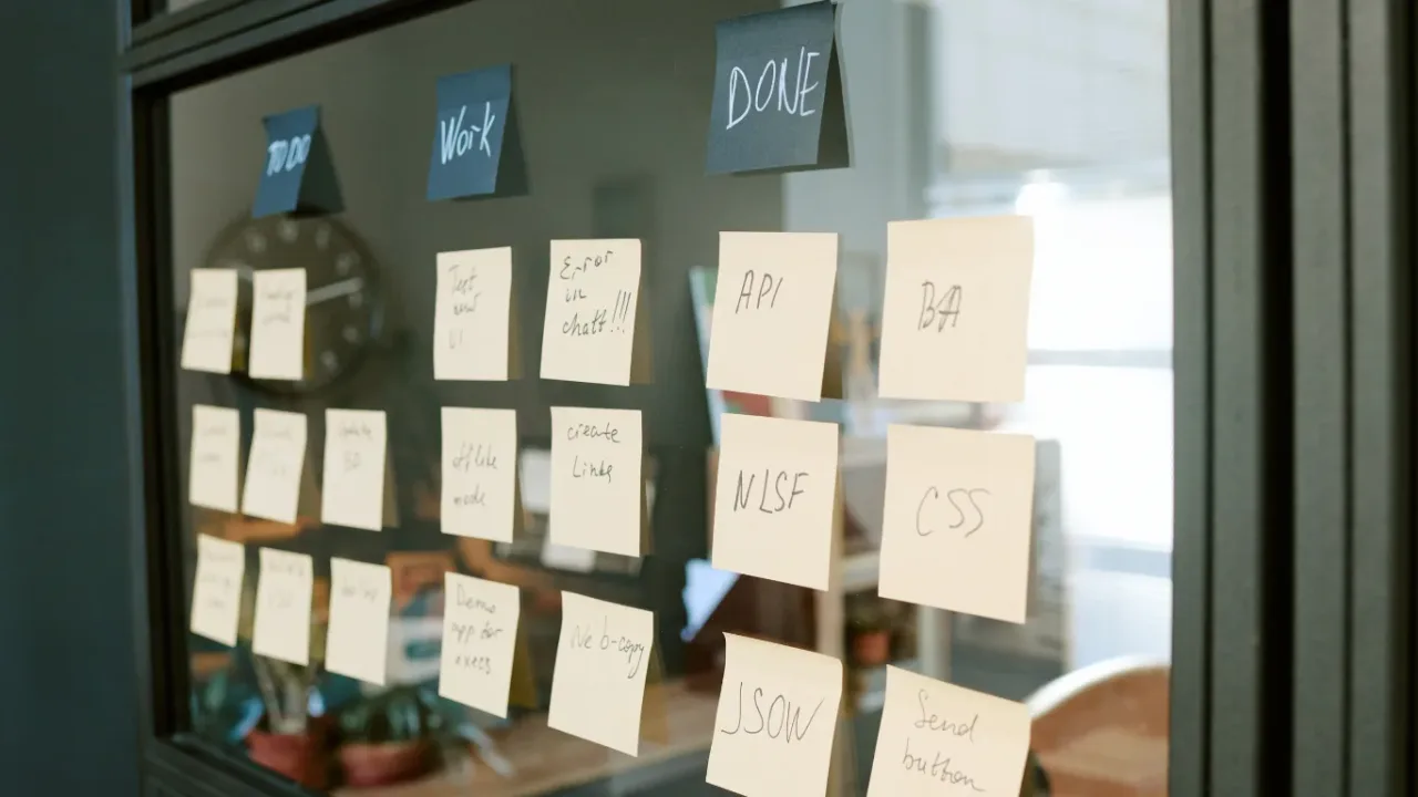 Task Manager board with sticky notes organized into workflow columns on a glass wall in a modern office.