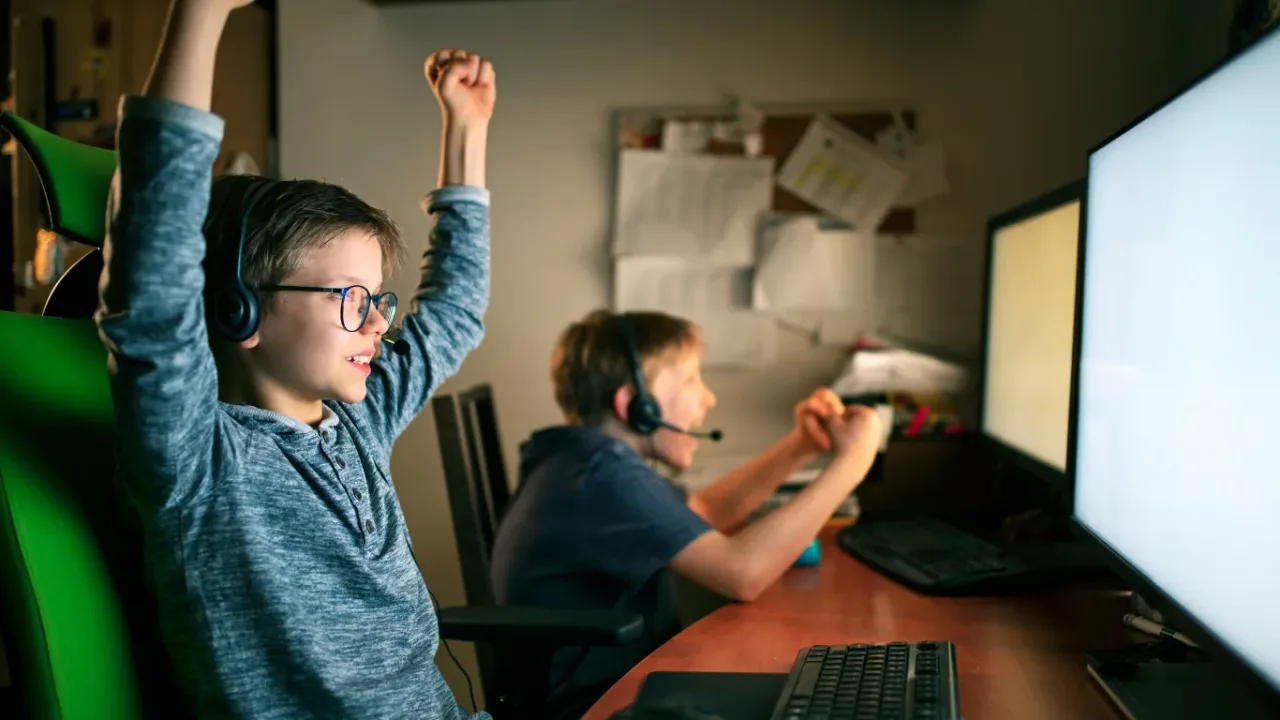 Two young gamers celebrating while playing Free PC Games on desktop computers.