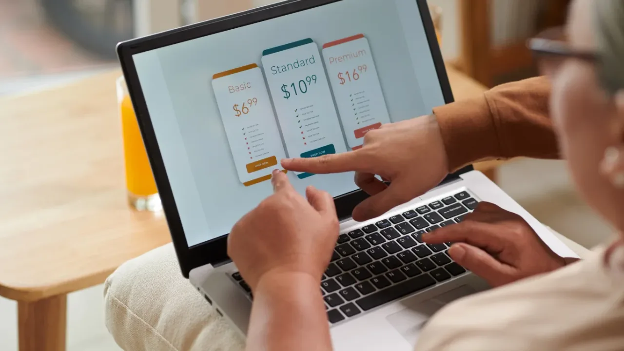 Game Subscription Services pricing plans displayed on a laptop screen as two people compare subscription options and select a plan.