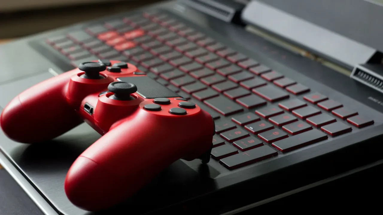 A red wireless game controller resting on the keyboard of a sleek Gaming Laptop, with black and red keys creating a modern gaming setup in a close-up view.