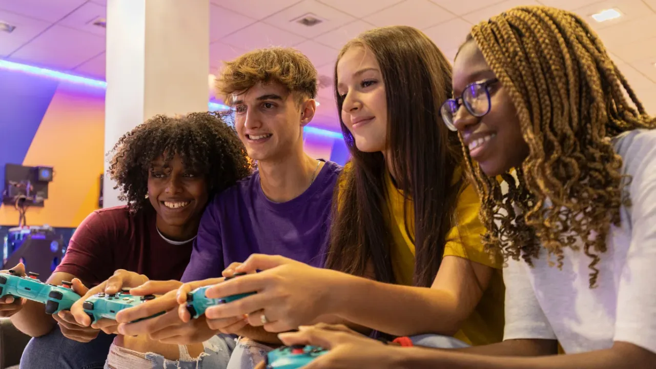 Friends playing a Multiplayer Game together with controllers in a colorful gaming lounge.