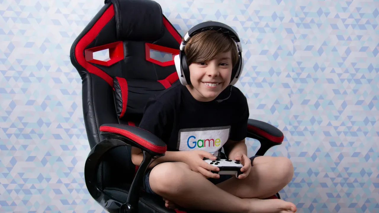 Smiling child wearing a gaming headset and holding a controller while sitting in a comfortable Gaming Chair.