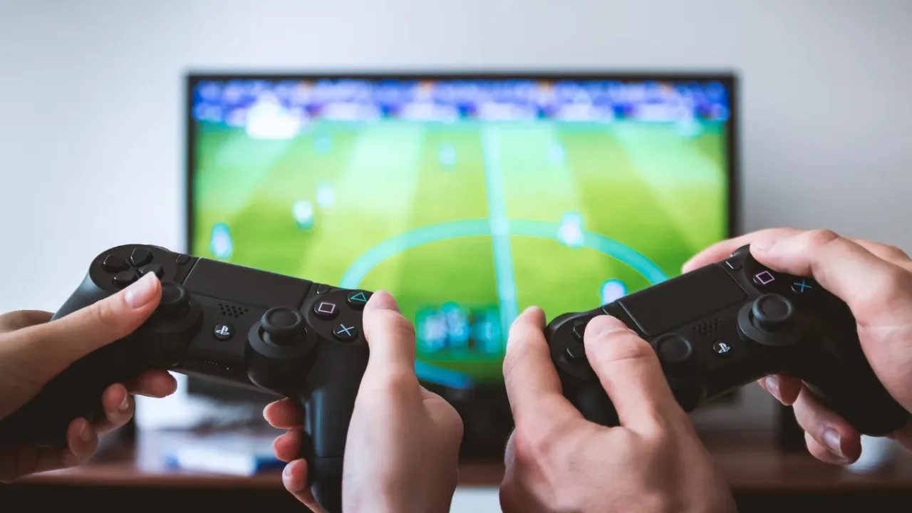 Two players holding controllers during a soccer video game, representing teamwork and competition within an Academy Team.