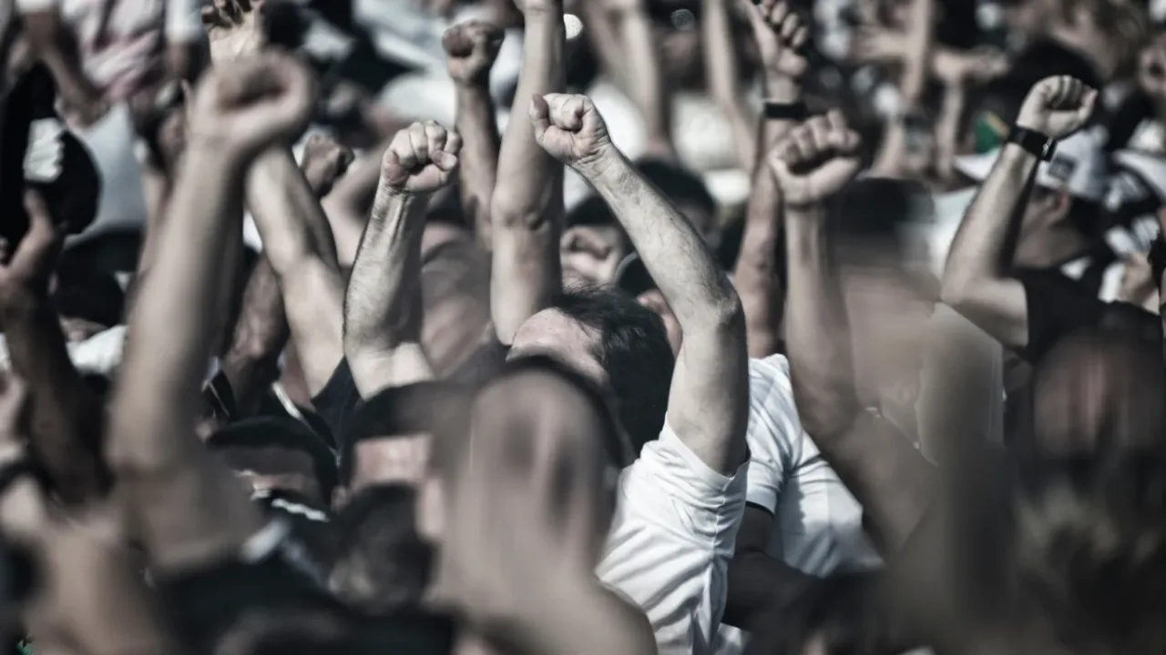 Capacity Standards represented by a large crowd of fans cheering with raised arms at a packed sporting event.