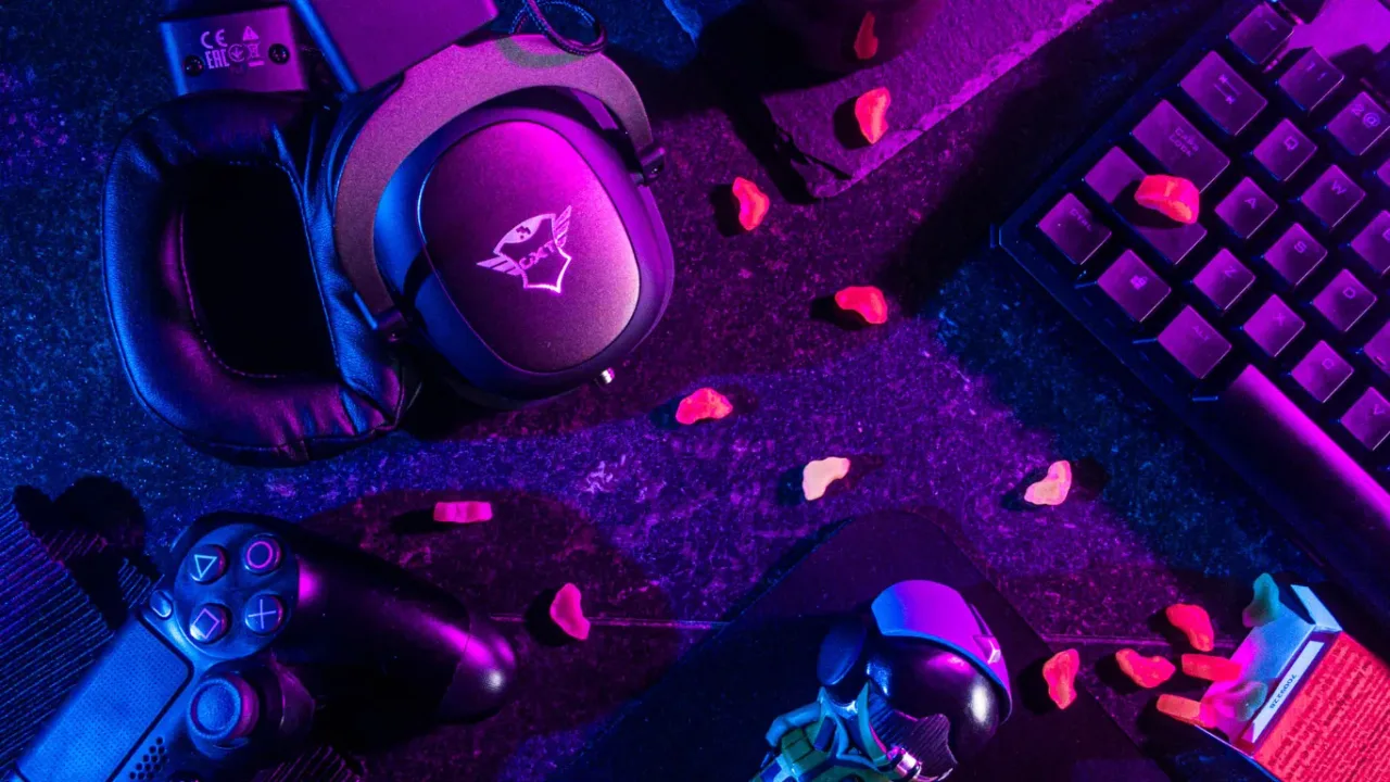 Gaming headset, controller, keyboard, and mouse illuminated by neon lights, representing a setup for adjusting gaming audio settings.
