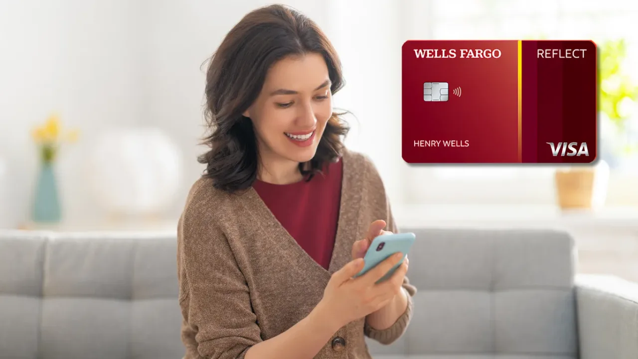 Woman in a brown cardigan smiling at her phone in a bright living room, with the Wells Fargo Reflect Visa credit card beside her.