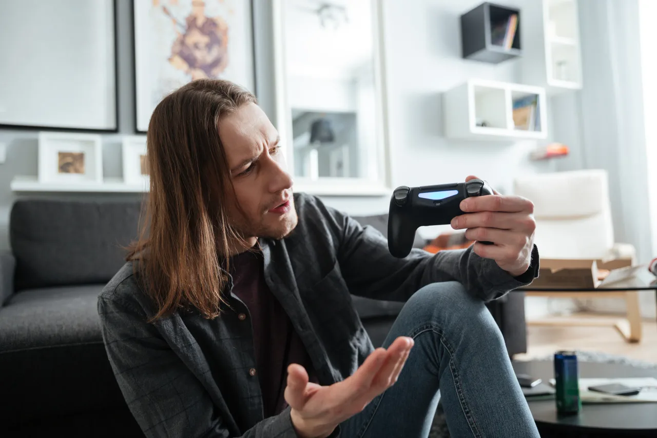 confused man sitting home indoors play games with joystick