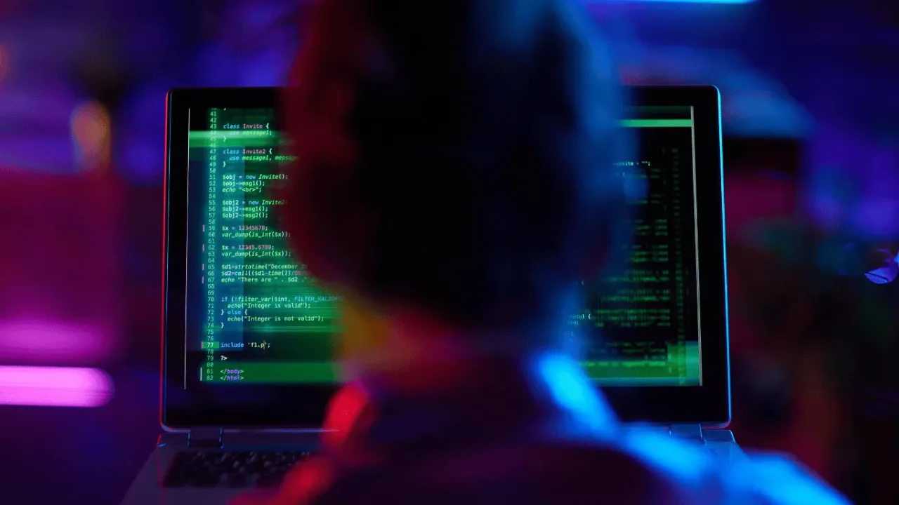 A developer focused on lines of complex code on a laptop screen, working late to secure user data through carefully configured Privacy Settings.