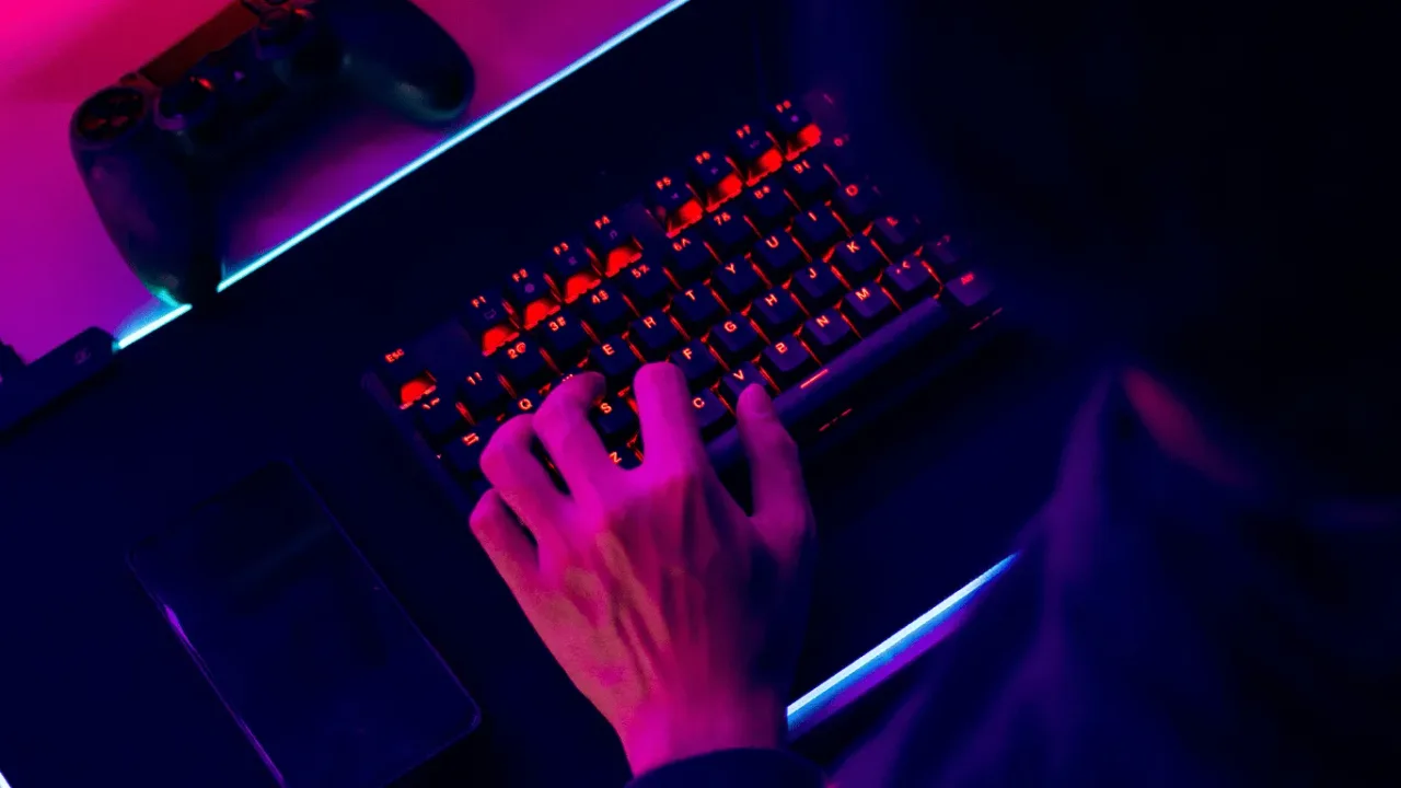 A gamer's hand typing on a mechanical keyboard illuminated by neon lighting, serving as a reminder to optimize Router Settings That Prioritize Gaming Traffic.