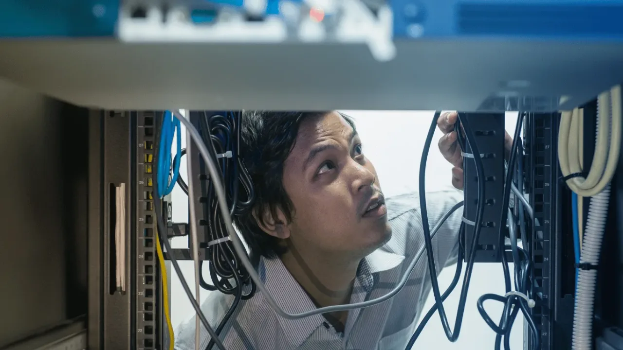 A technician meticulously inspects cables in a server rack, illustrating the precise Network Troubleshooting Steps for Consistent Ping needed for an optimized connection.
